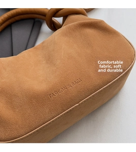 Detail van de bruine suède handtas met reliëftekst en een geknoopt handvatontwerp