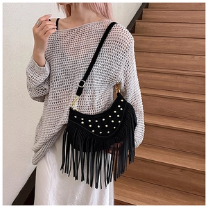 Detail of black suede crescent bag featuring golden rivets and long fringe tassels