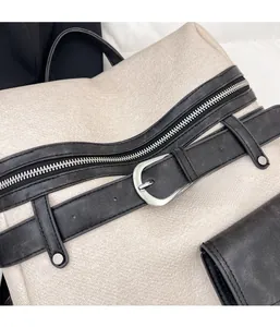 Detail of cream woven fabric backpack featuring a black leather strap and silver zipper