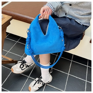 Detail of blue suede dumpling bag showing knot strap and soft matte texture