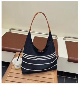 Detail of a navy striped canvas tote bag with brown leather strap on a wooden table
