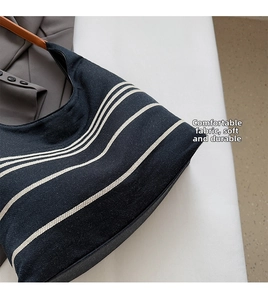 Close-up of black canvas tote with white stripes and brown leather strap detail