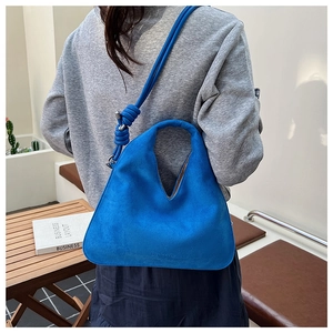 Blue suede hobo bag styled as a shoulder bag on a model in a minimalist cafe setting