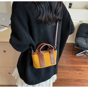 Primo piano di una piccola borsa a secchiello in tela bicolore portata a tracolla