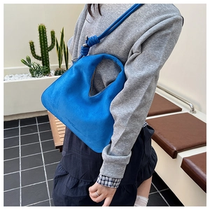 Detail of blue suede shoulder bag featuring a unique knotted strap and sleek curved design
