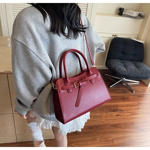 Close-up of a burgundy leather handbag with knot buckle detail shown in a home setting