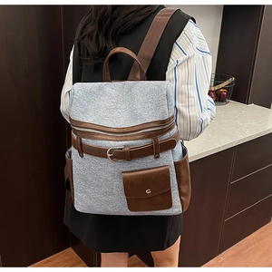 Detail of light blue denim texture backpack with brown leather straps and metal buckles