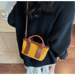 Detail of a mini yellow canvas tote bag with brown leather handles and slim shoulder strap