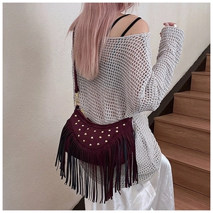 Detail of burgundy suede crossbody bag with golden rivets and long fringe tassel decoration