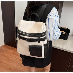 Side view of model wearing a large cream fabric commuter backpack with black leather accents