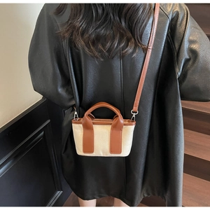 Detail of canvas handbag with brown leather trim and metal hook on model background