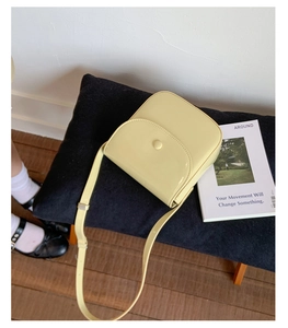 Gros plan d'un sac besace jaune pâle sur un banc en velours noir avec un rabat élégant
