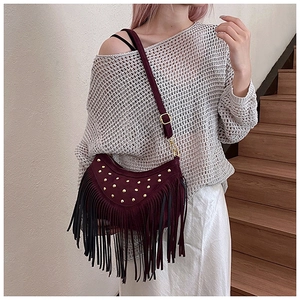 Close-up of burgundy suede crossbody bag with gold studs and long fringe tassels