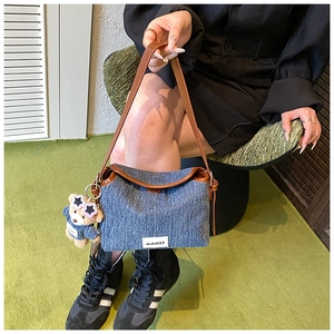 Detail of denim shoulder bag with brown leather straps and a cute teddy bear charm
