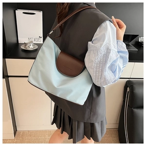 Detailed side view of a blue and brown contrast tote bag worn by a model in an office setting