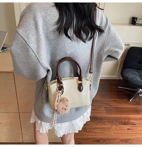 Detail view of cream crossbody bag with brown contrast handle and bear charm on a model