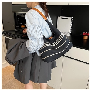 Detail of black nylon tote bag with white horizontal stripes and brown leather strap