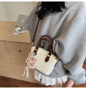 Detail der cremefarbenen Mini-Tasche mit braunem Griff und süßem Bären-Anhänger