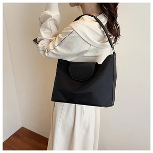 Minimalist black shoulder bag with textured flap and round shoulder strap side view