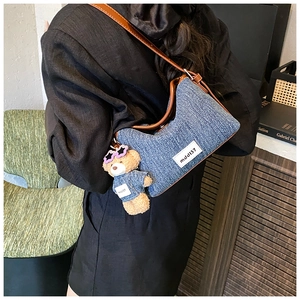 Close-up of denim shoulder bag with brown leather trim and a cute plush bear pendant