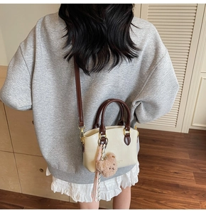 Detailed back view of a cream crossbody bucket bag with brown handle and bear charm