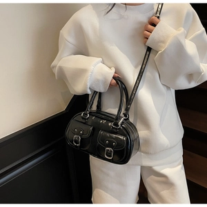 Detail of black patent leather bowling bag with silver buckles on white hoodie model