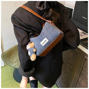 Detail of denim shoulder bag with leather trim and bear plush charm shown on model
