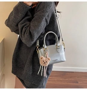 Details einer silbernen Metallic-Handtasche mit Plüschbär und goldener Hardware am Modell