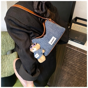 Detail of blue denim shoulder bag with brown leather strap and bear charm pendant