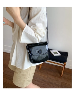 Détail d'un sac besace en cuir verni noir avec finition brillante et boucle ronde