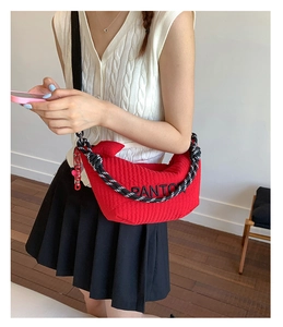 Detailed view of red quilted hobo bag with striped strap and pink chain ornament