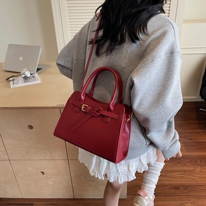 Détail du sac cabas en cuir rouge avec sangle nouée et boucle dorée dans un bureau
