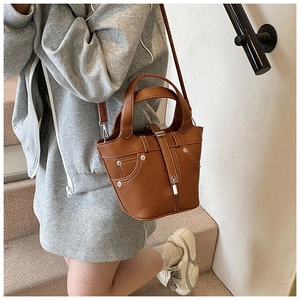 Sac seau marron en cuir grainé avec coutures contrastées porté par un mannequin chic