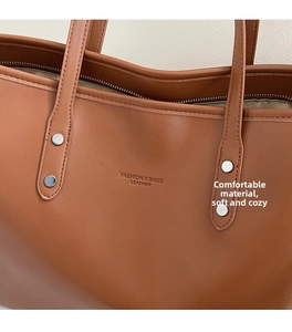 Close-up of brown leather tote bag featuring embossed logo and silver rivet strap details