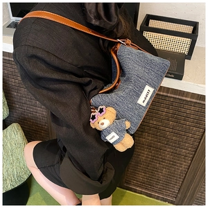 Detail of denim bucket bag with brown leather strap and mini teddy bear keychain