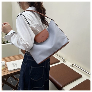 Detail of light blue tote bag with brown leather contrast stitching and metal brand logo
