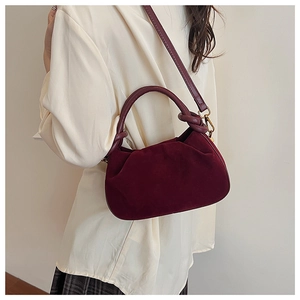 Detail van bordeauxrode geplooide tas met gedraaide handvatten en zachte matte textuur