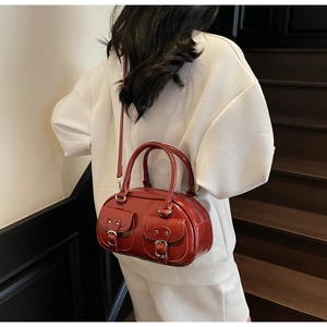 Detail of red glossy leather barrel handbag with decorative pockets and top handles