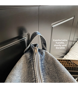 Détail du sac fourre-tout en jean lavé montrant le tissu, le zip et la poignée solide