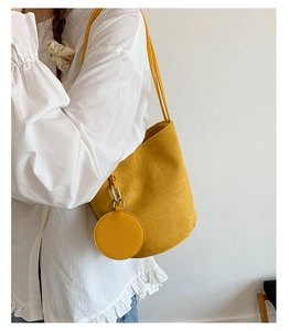 Detail of yellow suede bucket bag with round coin purse charm on white shirt background