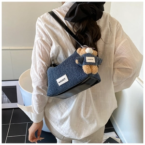Detail of denim shoulder bag with brand patch and cute plush bear charm accessory