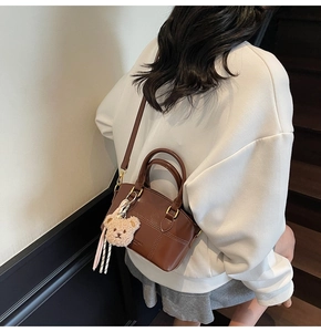 Detailed shot of brown PU leather crossbody bucket bag with plush bear charm and tassels