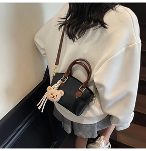 Detail der schwarzen Leder-Eimertasche mit braunen Griffen und Plüschbär-Anhänger