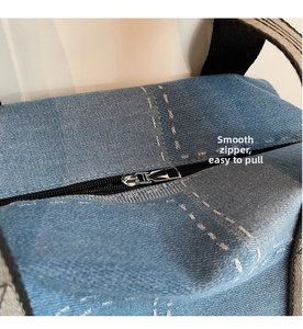Detailed close-up of the smooth metal zipper and white stitching on a denim tote bag