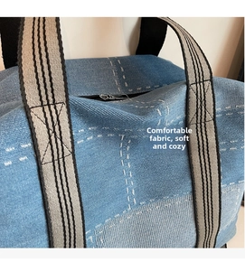 Detail of blue denim tote bag featuring white grid stitching and striped woven handles