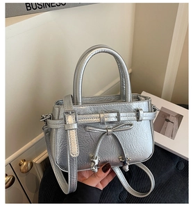 Détail d'un mini sac argenté avec texture métallique, nœud et pendentifs étoiles