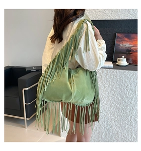 Side view of a light green suede tote bag with long fringe details and a bohemian style