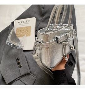 Detail of silver metallic handbag with wave texture and premium hardware on grey fabric