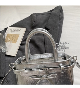 Detail of silver metallic handbag with bow accent and inner zipper pocket displayed on a book