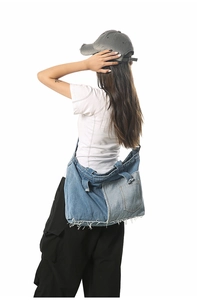 Detail of a large patchwork denim tote bag with frayed edges and belt buckle accents